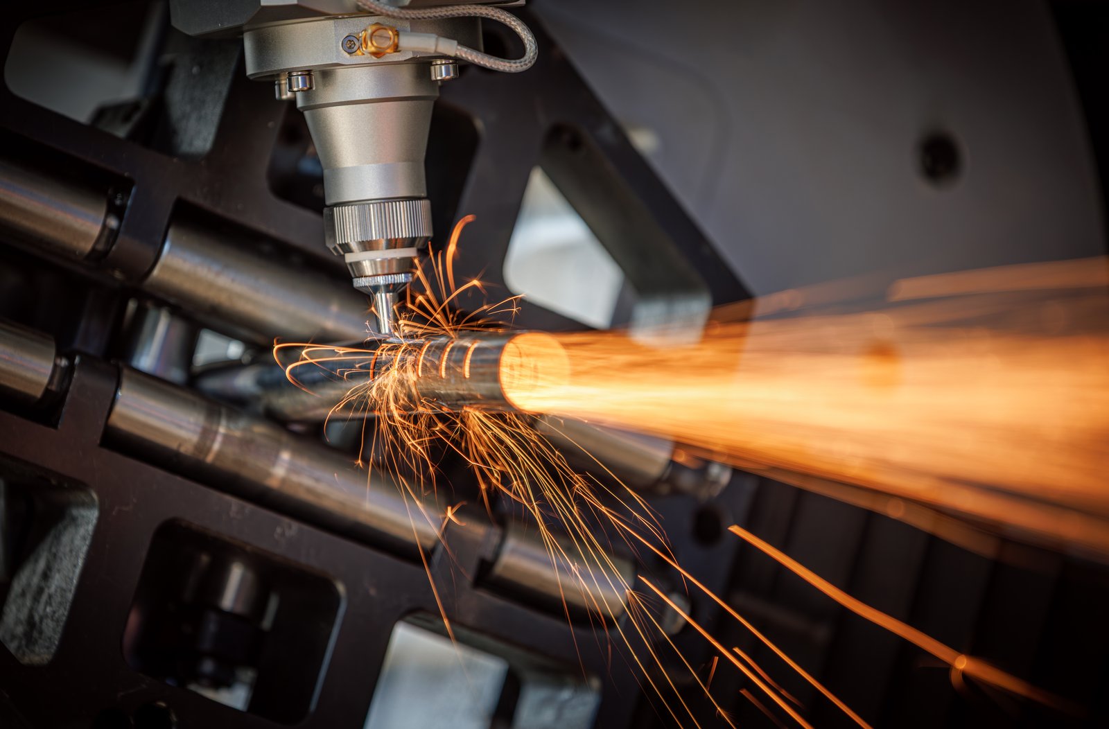 Detailed shot of laser head cutting a rotating pipe section with high-speed linear sparks. Shows powerful CNC control and stable clamping.