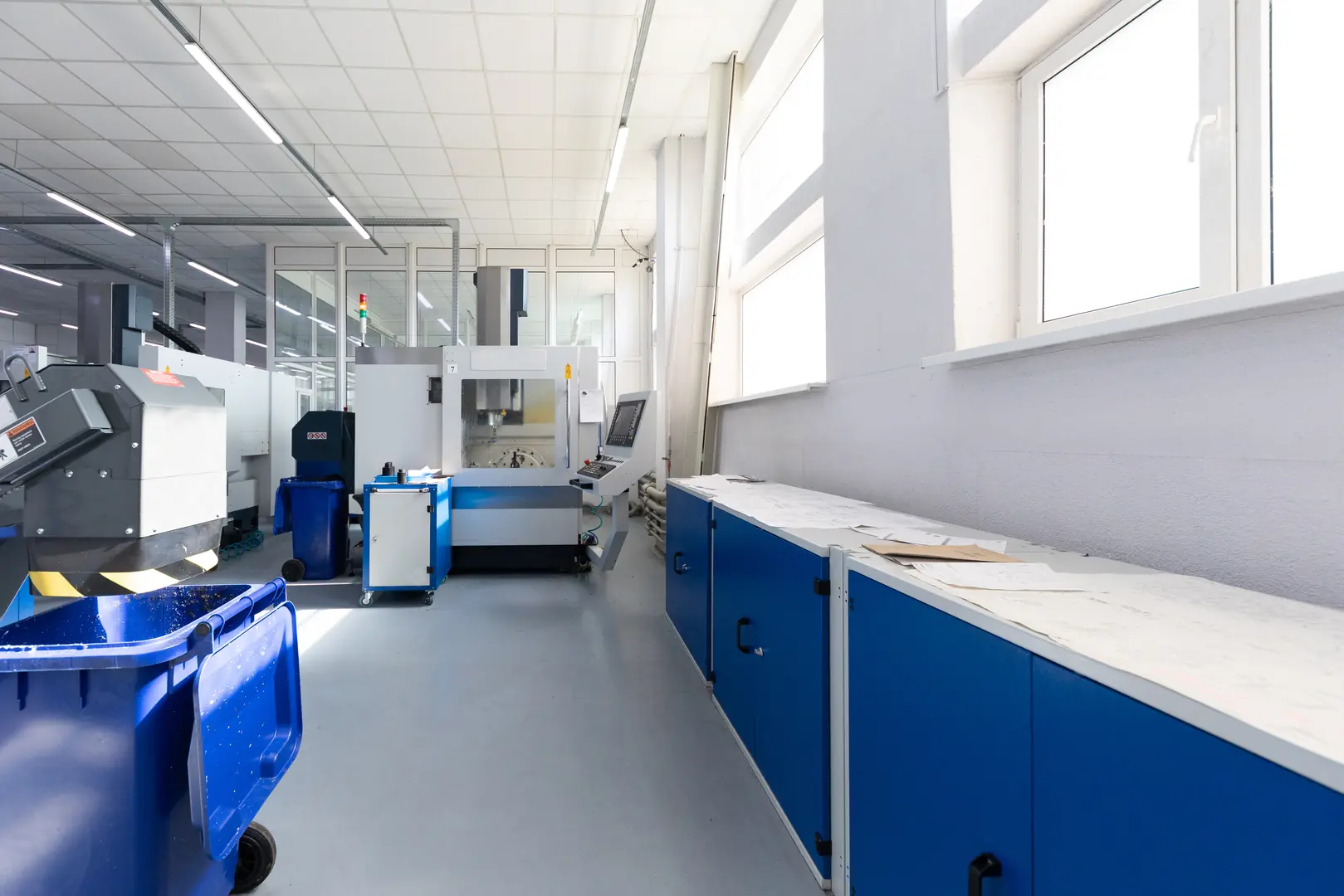 Modern laser cutting machine setup in a clean, organized industrial workshop with blue cabinets and large windows.